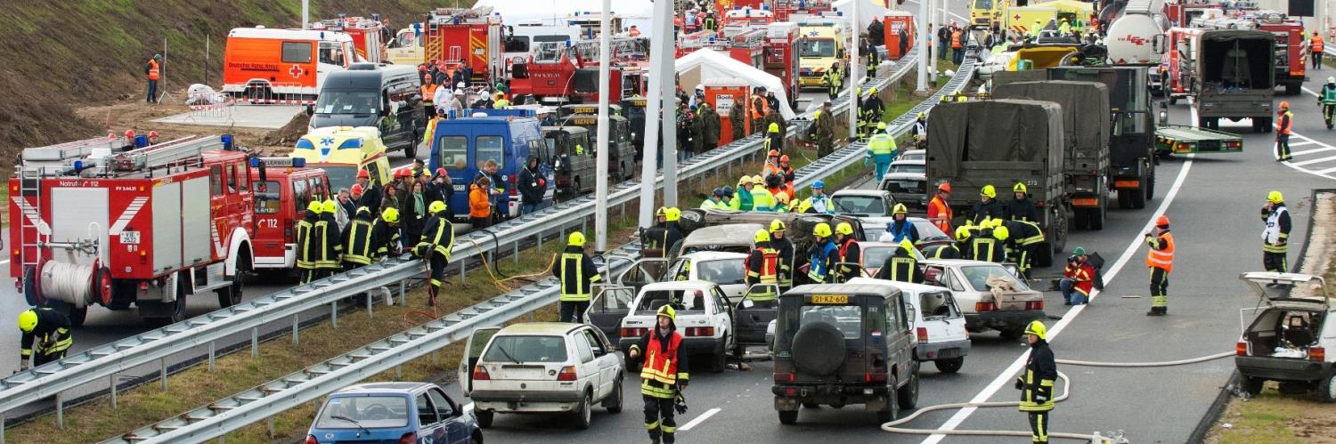 Snelweg waarbij allebei de rijrichtingen bezet zijn door meerdere brandweerwagens en ambulances en brandweermannen op de weg lopen om hulp te verlenen